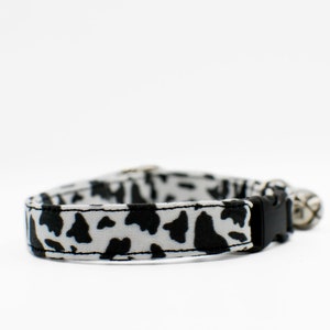 Peut inclure: Un collier de chat imprim&eacute; vache noir et blanc avec une boucle noire et une clochette argent&eacute;e.