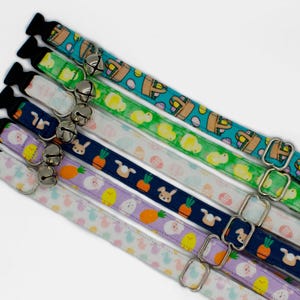 May include: A set of seven colorful cat collars with different Easter-themed patterns, including bunnies, eggs, and carrots. Each collar has a silver buckle and a bell.