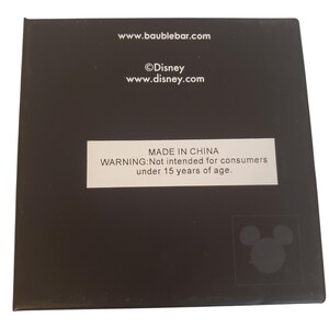 K&ouml;nnte beinhalten: Eine schwarze quadratische Box mit wei&szlig;em Text und einem Disney-Logo. Der Text enth&auml;lt Website-Adressen f&uuml;r Baublebar und Disney sowie einen Hinweis, dass das Produkt nicht f&uuml;r Verbraucher unter 15 Jahren bestimmt ist.
