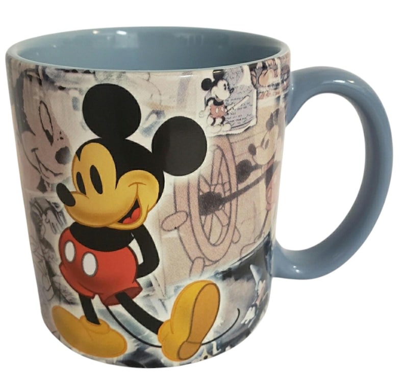 May include: A ceramic mug featuring Mickey Mouse. The mug has a light blue interior and handle. The exterior showcases a collage of Mickey Mouse sketches and illustrations, with a large image of Mickey in his classic outfit.