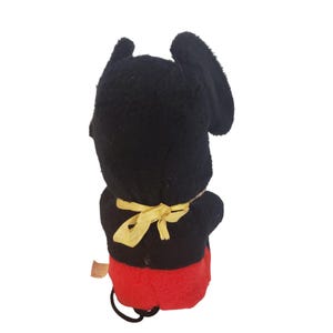 Op de afbeelding: Vintage Mickey Mouse pluche speelgoed. Het pluche heeft een zwarte kop en oren, een zwart lichaam, rode shorts en een gele strik. Het speelgoed is gemaakt van een zacht, pluche materiaal en heeft een aangehecht label.
