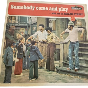 Peut inclure: Pochette d'album vinyle vintage de Sesame Street avec un groupe de personnes et d'enfants dansant dans la rue. Le titre de l'album, "Somebody Come and Play", est dans une bannière rouge. Le logo Sesame Street est visible.