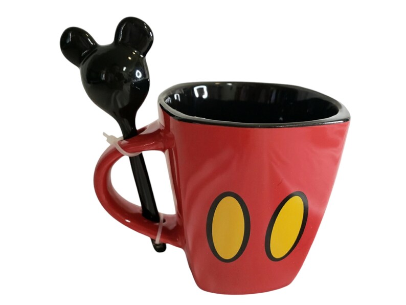May include: A red ceramic mug with a black interior and two yellow oval shapes on the front. The mug features a handle with an attached black spoon that has a handle shaped like the silhouette of a mouse head with two round ears.