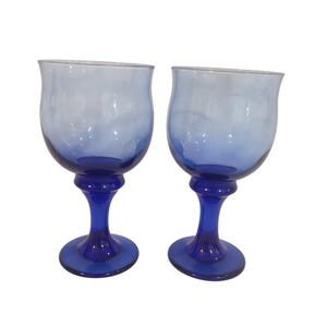 Puede incluir: Dos copas de cristal a juego, con una base y un tallo de color azul cobalto intenso que se transforman en un cuenco de color azul translúcido más claro. Cada copa tiene una forma redondeada de borde ancho y una base sólida.