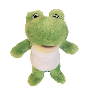 May include: A plush frog hand puppet featuring soft light green fur, a white belly, and a pale yellow throat area. The puppet has large, expressive embroidered eyes with black pupils and white highlights, designed for interactive play and storytelling.