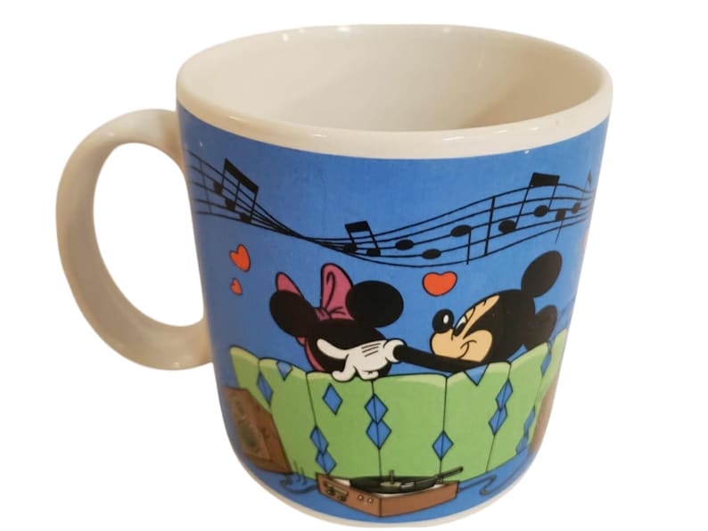 K&ouml;nnte beinhalten: Keramik-Kaffeetasse mit Mickey und Minnie Mouse in einer romantischen Szene. Die Tasse hat einen blauen Hintergrund mit Noten und Herzen. Der Griff und das Innere sind wei&szlig;. Das Design beinhaltet einen Plattenspieler.