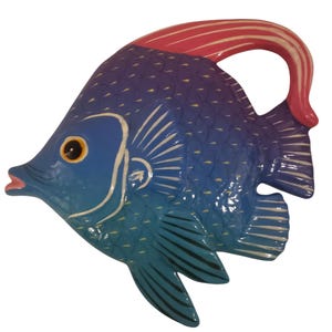 May include: A hand-painted, wooden fish sculpture in shades of blue, purple, and teal. The fish has a red and white fin and a yellow eye. The sculpture is a decorative item.