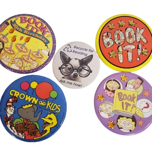 Puede incluir: Un conjunto de botones redondos y coloridos con varios diseños. Uno dice "BOOK IT!" con estrellas, otro presenta un perro con gafas, y otros tienen personajes de dibujos animados y texto como "Crown Kids" y "Book It! 40th Birthday".
