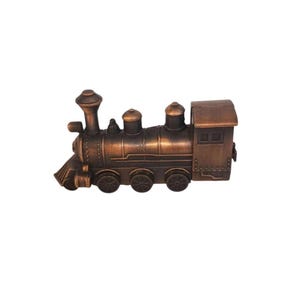 May include: A bronze-colored miniature train engine with detailed features, including a smokestack, dome, and wheels. The toy train is a decorative item, likely a collectible or a piece of home decor.