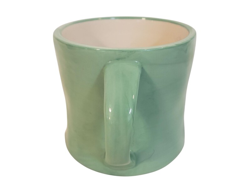 May include: A handmade ceramic mug in a soft, muted green color. The mug has a rounded shape with a sturdy handle and a contrasting off-white interior. This unique mug is perfect for enjoying your favorite hot beverages.