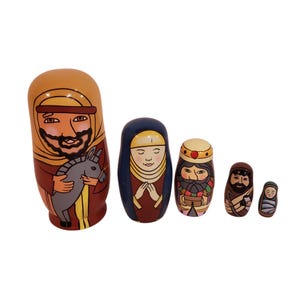May include: A set of five wooden nesting dolls depicting a nativity scene. The largest doll is a man holding a donkey, followed by a woman, two men, and a baby. The dolls are painted with detailed faces and clothing in various colors.
