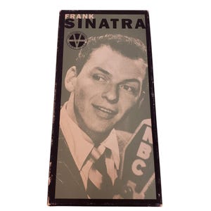 Puede incluir: Una portada de álbum vintage de Frank Sinatra. La portada presenta una imagen en blanco y negro de Frank Sinatra con traje y corbata, sosteniendo un micrófono. El título del álbum "Frank Sinatra" está impreso en letras negras en negrita en la parte superior.