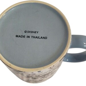 May include: A blue ceramic mug with a matching handle. The bottom of the mug is light blue and features the text "&copy; DISNEY MADE IN THAILAND". The mug has a white and gray design on the exterior.