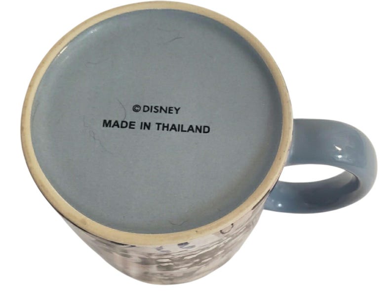 May include: A blue ceramic mug with a matching handle. The bottom of the mug is light blue and features the text "&copy; DISNEY MADE IN THAILAND". The mug has a white and gray design on the exterior.
