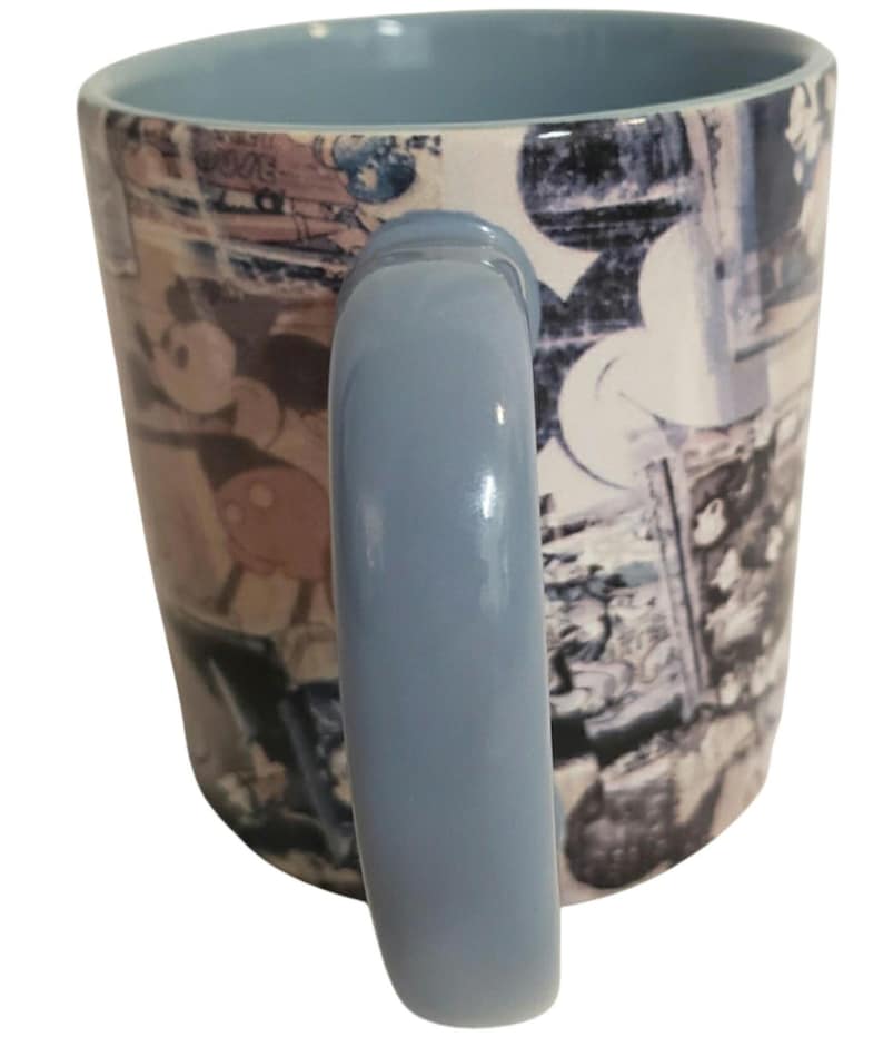 May include: A ceramic mug with a light blue handle and interior. The exterior features a collage of images, including a cartoon character. The mug is white with blue and brown accents.