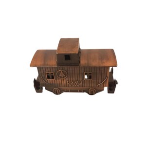 May include: A bronze-colored miniature train caboose with a small cabin on top. The caboose has windows and the text "LS&S 4348" on the side, along with a tree emblem. The model is detailed with grooves and rivets.