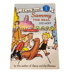 Puede incluir: Portada del libro infantil "Sammy the Seal" de Syd Hoff. La ilustración muestra una foca caminando con niños, con un fondo de ciudad y el texto "I Can Read!" en la parte superior.