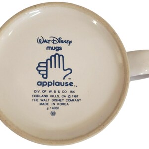 K&ouml;nnte beinhalten: Ein Set aus drei Keramikbechern mit einer gesprenkelten, cremefarbenen Glasur. Jeder Becher hat ein anderes handgemaltes Design: ein blaues und gr&uuml;nes Blatt, eine gelbe Blume und eine rote Beere. Die Becher haben ein schlichtes, modernes Design.