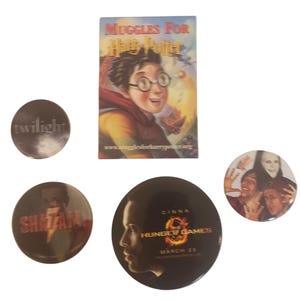 Könnte beinhalten: Sammlung von runden Buttons und einem kleinen Poster. Die Buttons zeigen die Texte "Twilight", "Shazam" und "Hunger Games". Das Poster ist für "Muggles for Harry Potter".