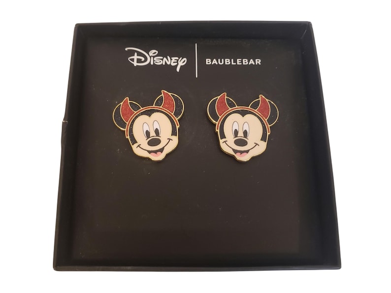 K&ouml;nnte beinhalten: Zwei Mickey-Mouse-Gesicht-Anstecknadeln in einer schwarzen Schachtel. Die Anstecknadeln haben einen goldenen Umriss, einen rot-schwarzen Hut und ein l&auml;chelndes Gesicht. Die Schachtel tr&auml;gt die Logos von Disney und Baublebar.