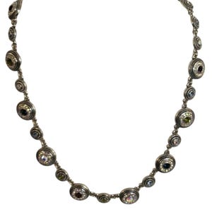 May include: Silver necklace with a series of circular gemstones in various colours. The necklace has a delicate chain with alternating small and large gemstone settings. The gemstones include clear, green, blue, and red stones.