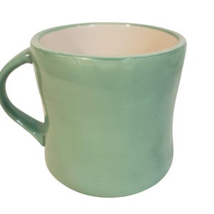 May include: A light green ceramic mug with a curved body and a handle. The interior of the mug is white. The mug is designed with a smooth, glossy finish. This mug is suitable for hot or cold beverages.