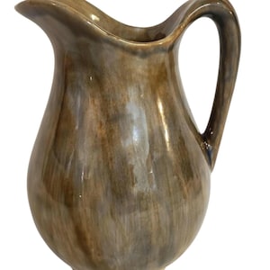 Könnte beinhalten: Eine braune Keramikkrug mit einem gebogenen Griff und einem Ausguss. Der Krug hat eine glänzende Oberfläche und ein marmoriertes Aussehen mit Braun- und Beigetönen. Der Krug ist ein dekorativer Gegenstand.