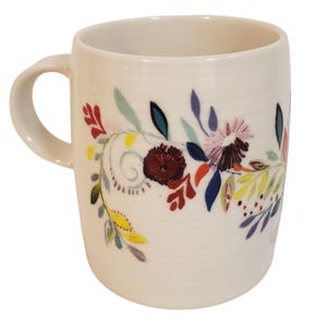 May include: Cream-colored ceramic mug with a curved handle. The mug is decorated with a floral design featuring burgundy, pink, blue, and yellow flowers and leaves. The design wraps around the mug's exterior.