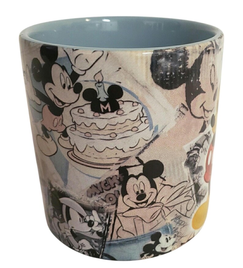 May include: A ceramic tumbler featuring a light blue interior and a wrap-around design with Mickey Mouse illustrations. The design includes images of Mickey Mouse, a birthday cake, and the word "Mickey".