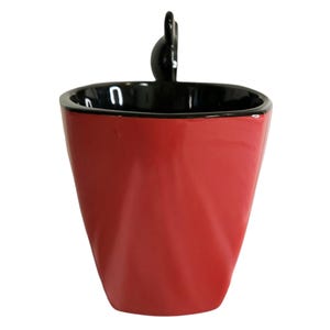 May include: A glossy red ceramic mug with a black interior and a black rim. The mug features a tapered, faceted body design and a small, black, rounded handle extending from the top edge, creating a distinct silhouette against a white background.