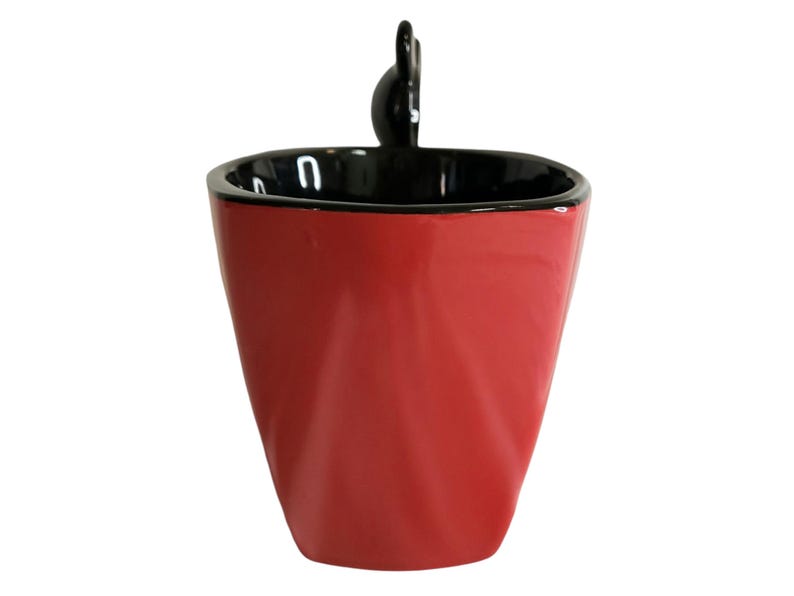 May include: A glossy red ceramic mug with a black interior and a black rim. The mug features a tapered, faceted body design and a small, black, rounded handle extending from the top edge, creating a distinct silhouette against a white background.