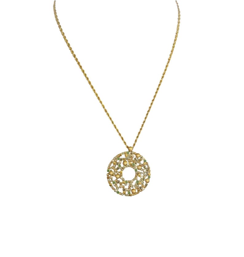 May include: Gold-coloured necklace with a circular pendant. The pendant has an openwork design and is embellished with yellow and green gemstones. The chain is a delicate rope style, suitable for everyday wear.