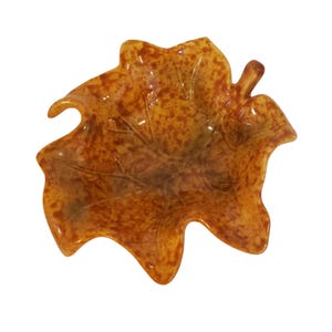 May include: A decorative leaf-shaped dish in shades of amber and brown. The dish has a glossy finish and a speckled pattern, with leaf vein details. The dish is a unique accent piece for home decor.