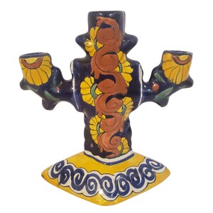 May include: A ceramic candelabra featuring a deep blue base color with hand-painted yellow sunflower motifs and a central vertical brown scroll design. The base is yellow with a blue swirling pattern, and it holds three candles in total.