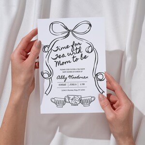 May include: A monochrome baby shower invitation featuring the text "Time for Tea with Mom to be". The invitation includes the name "Ally Woodman", event details, and illustrations of ribbons and teacups. The design is in black and white.