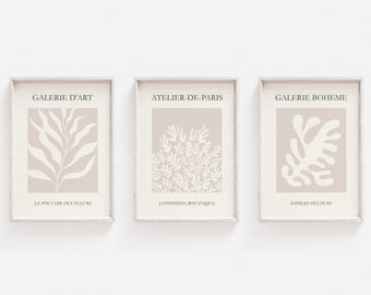 May include: Three framed prints with a beige background and white abstract floral designs. The top of each frame has text in black: "GALERIE D'ART", "ATELIER-DE-PARIS", and "GALERIE BOHEME". Below the floral designs, each frame has text in black: "LE POUT DIK DES FLEUKE", "EXPOSTIION BOTANIQUE", and "PAPIERS DECOUPE".