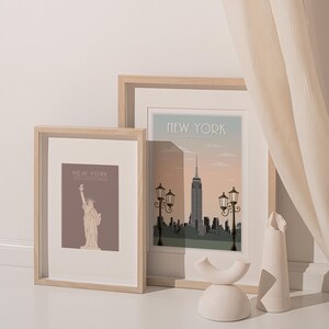 May include: Two framed prints of New York City landmarks. The left print features a brown background with a line drawing of the Statue of Liberty. The right print features a skyline with the Empire State Building and streetlights. Both prints have a light wood frame.