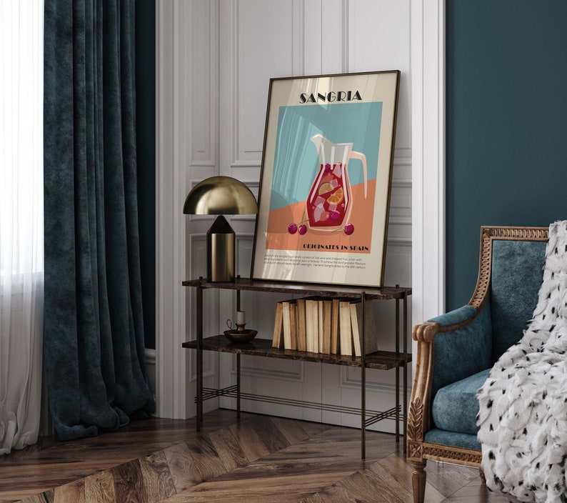 May include: A framed art print featuring a Sangria illustration with a pitcher, fruit, and the text "Sangria" and "Originates in Spain." The artwork is displayed on a dark brown shelf with a gold lamp and books. The room has teal curtains and a blue armchair.