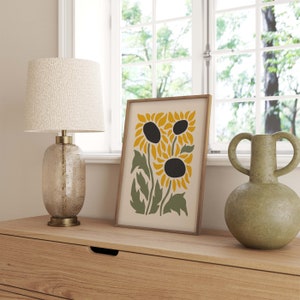 May include: A framed print of a stylized sunflower design with three sunflowers in shades of yellow and green on a cream background.