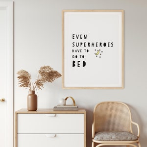 Puede incluir: Una impresi&oacute;n enmarcada con fondo blanco y texto negro que dice "Incluso los superh&eacute;roes tienen que irse a la cama". El texto est&aacute; en una fuente l&uacute;dica e incluye una luna creciente amarilla y estrellas.
