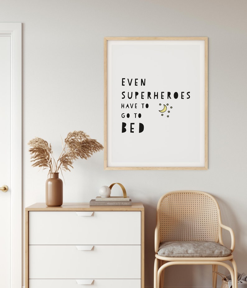 Puede incluir: Una impresi&oacute;n enmarcada con fondo blanco y texto negro que dice "Incluso los superh&eacute;roes tienen que irse a la cama". El texto est&aacute; en una fuente l&uacute;dica e incluye una luna creciente amarilla y estrellas.