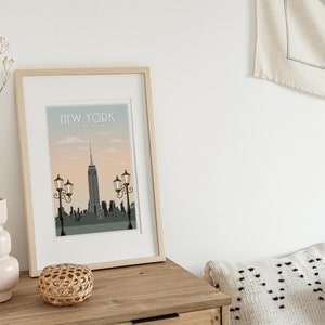 Puede incluir: Una impresi&oacute;n enmarcada con una ilustraci&oacute;n de la ciudad de Nueva York. La impresi&oacute;n tiene un fondo azul claro con una puesta de sol rosa y el texto "NEW YORK" en la parte superior.