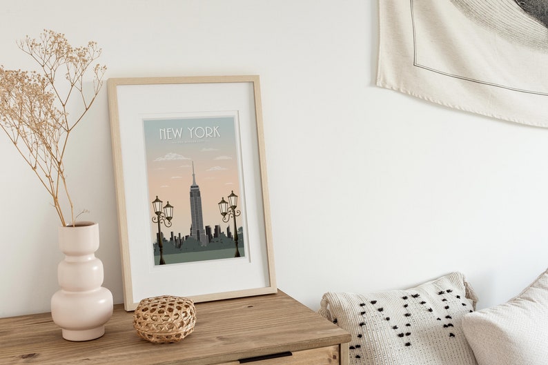 Puede incluir: Una impresi&oacute;n enmarcada con una ilustraci&oacute;n de la ciudad de Nueva York. La impresi&oacute;n tiene un fondo azul claro con una puesta de sol rosa y el texto "NEW YORK" en la parte superior.