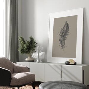 May include: A white cabinet with two doors and a white framed print of a black feather on a beige background. There are two white statues and a potted plant on top of the cabinet.