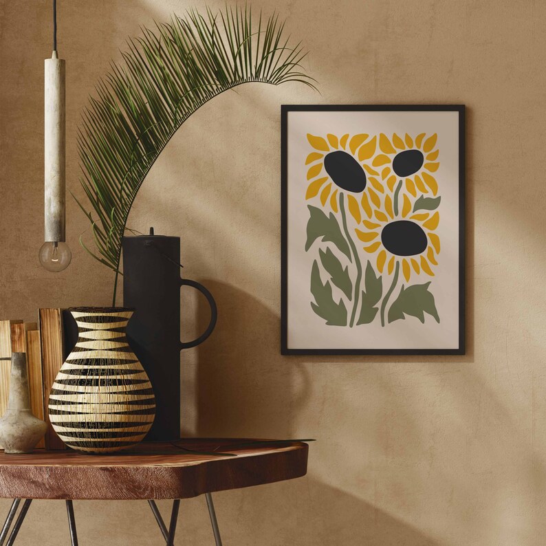 May include: A framed print of three stylized sunflowers in yellow and green on a cream background. The sunflowers have black centers and are arranged in a cluster.
