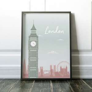 May include: Framed art print featuring a stylized illustration of London landmarks. The artwork includes Big Ben, the London Eye, and other buildings in shades of gray and pink against a light blue background. The word "London" is written in white.