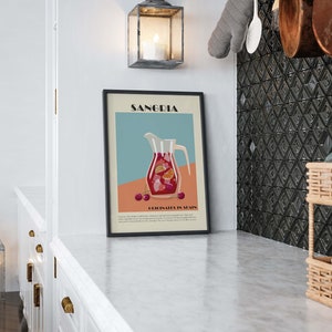 May include: A framed art print featuring a Sangria illustration. The artwork depicts a pitcher filled with red sangria, fruit slices, and cherries, set against a teal and peach background. The print is displayed in a kitchen setting.
