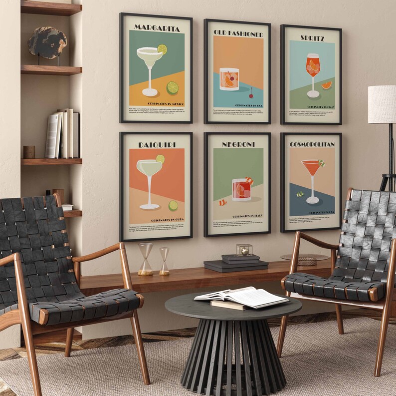 May include: Seven framed cocktail art prints, including Margarita, Old Fashioned, and Daiquiri, hang on a wall. Each print features a colorful, minimalist design of the cocktail with its name and origin. The artwork is displayed in a living room setting with chairs and a coffee table.
