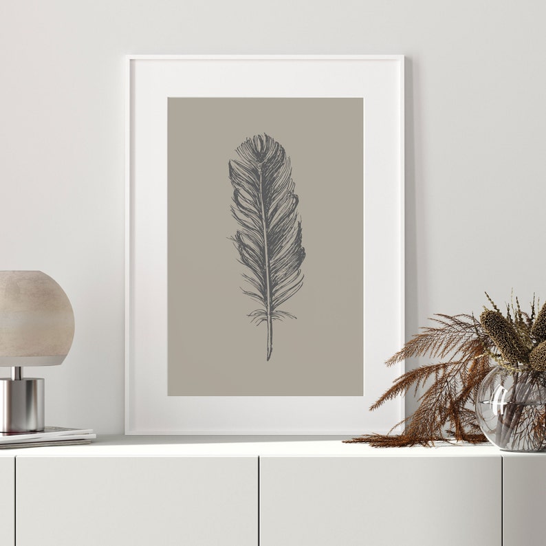 May include: A framed print of a black and white illustration of a single feather on a light brown background.