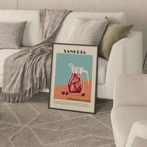 May include: A framed art print featuring a Sangria illustration. The artwork depicts a pitcher filled with red sangria, garnished with orange slices and cherries. The print has the word "Sangria" at the top and "Originates in Spain" at the bottom.